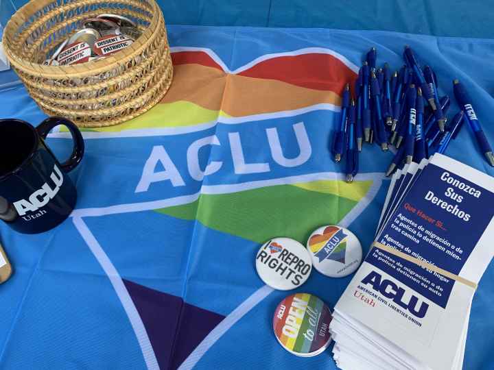 A photo of a table at Utah Pride with a table cloth that is a rainbow heart with ACLU in the center.