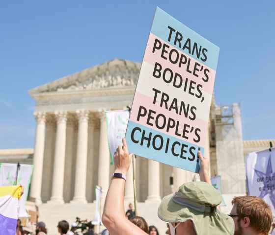 A demonstrator at a march in front of the Supreme Court holds up a sign reading "TRANS PEOPLE'S BODIES, TRANS PEOPLE'S CHOICES".